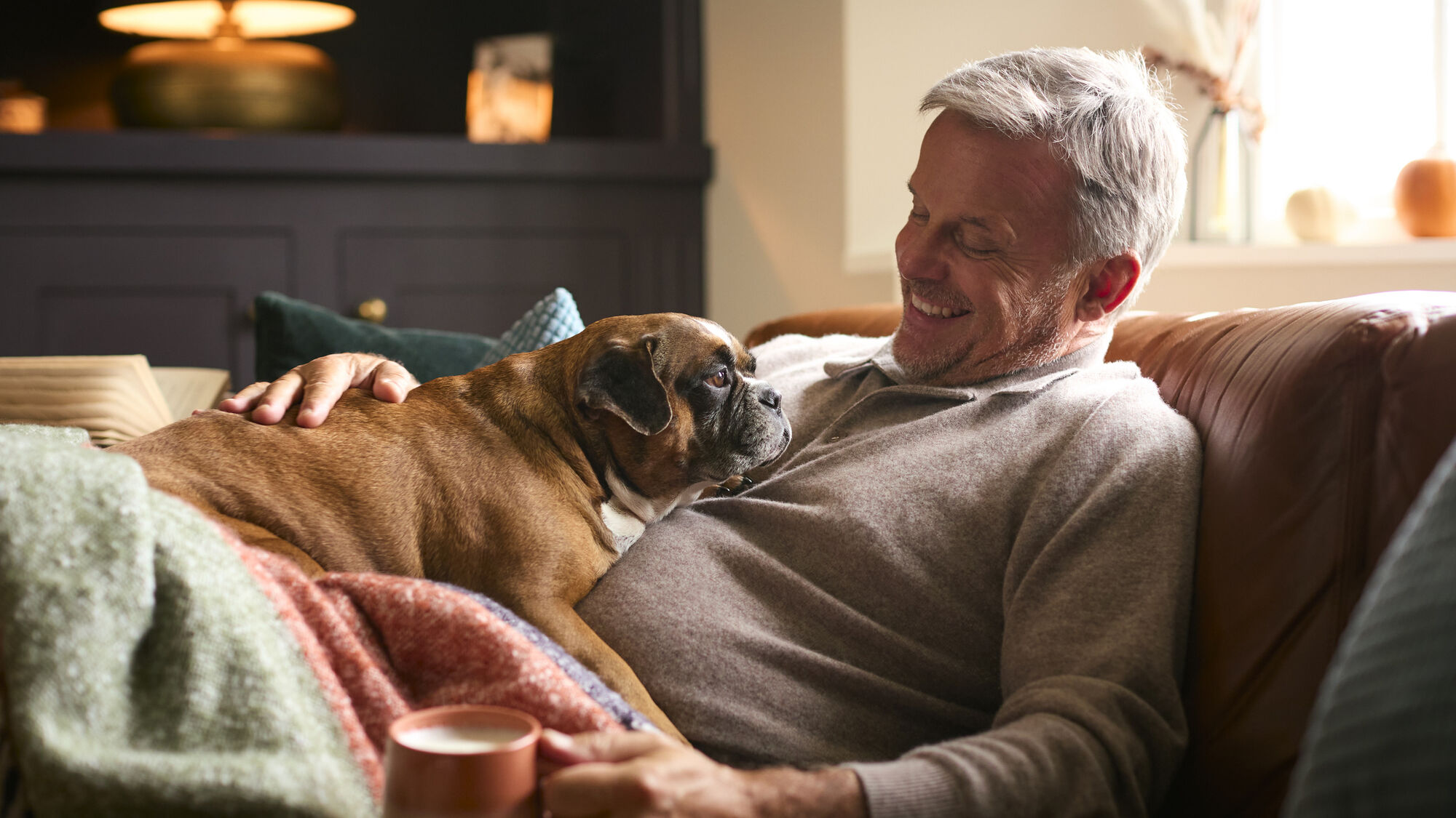Middle aged man with a cute dog on his lap, cozied up for winter with a blanket and hot cocoa.