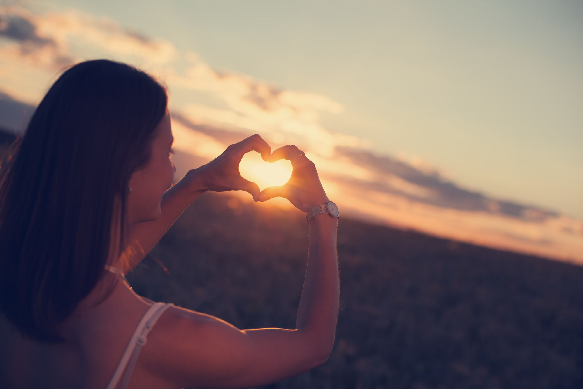 Woman making a heart with her hands around the sunset